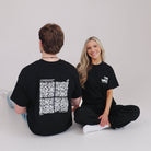 Two people wearing black t-shirts with QR code designs on a plain background